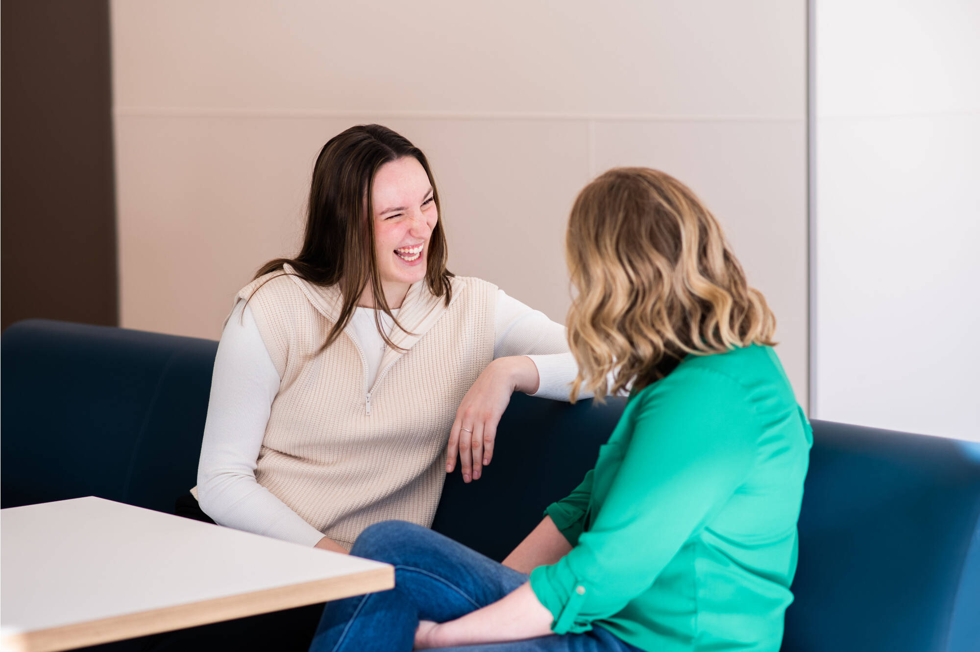two women sitting with each other, one facing camera laughing. the other facing away from camera
